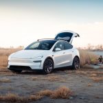 Tesla blanco junto al agua con el portón abierto en una escena de aventura al aire libre