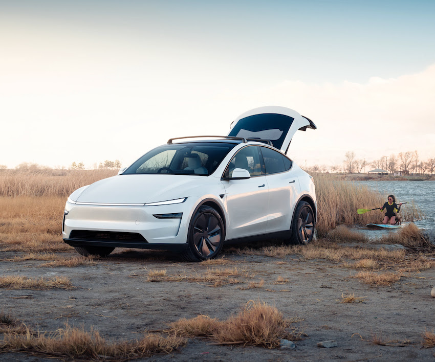 Tesla blanco junto al agua con el portón abierto en una escena de aventura al aire libre